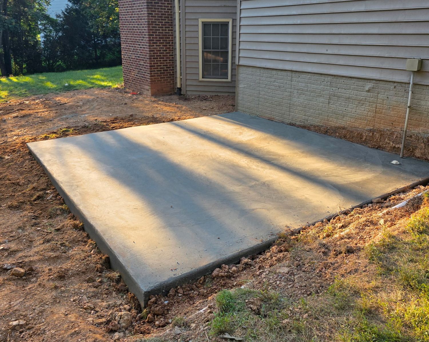 Freshly poured concrete pad against the back of a home