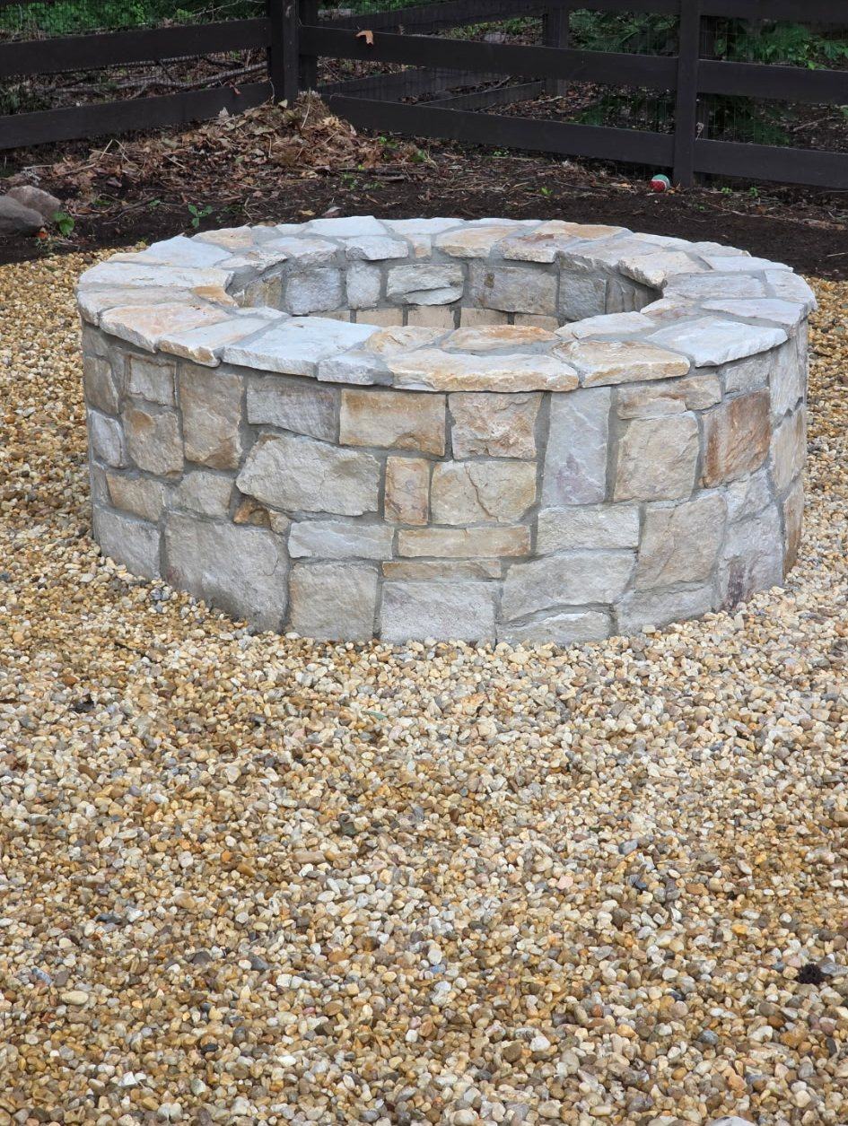 Round natural stone fire pit with a flat stone cap set in river gravel