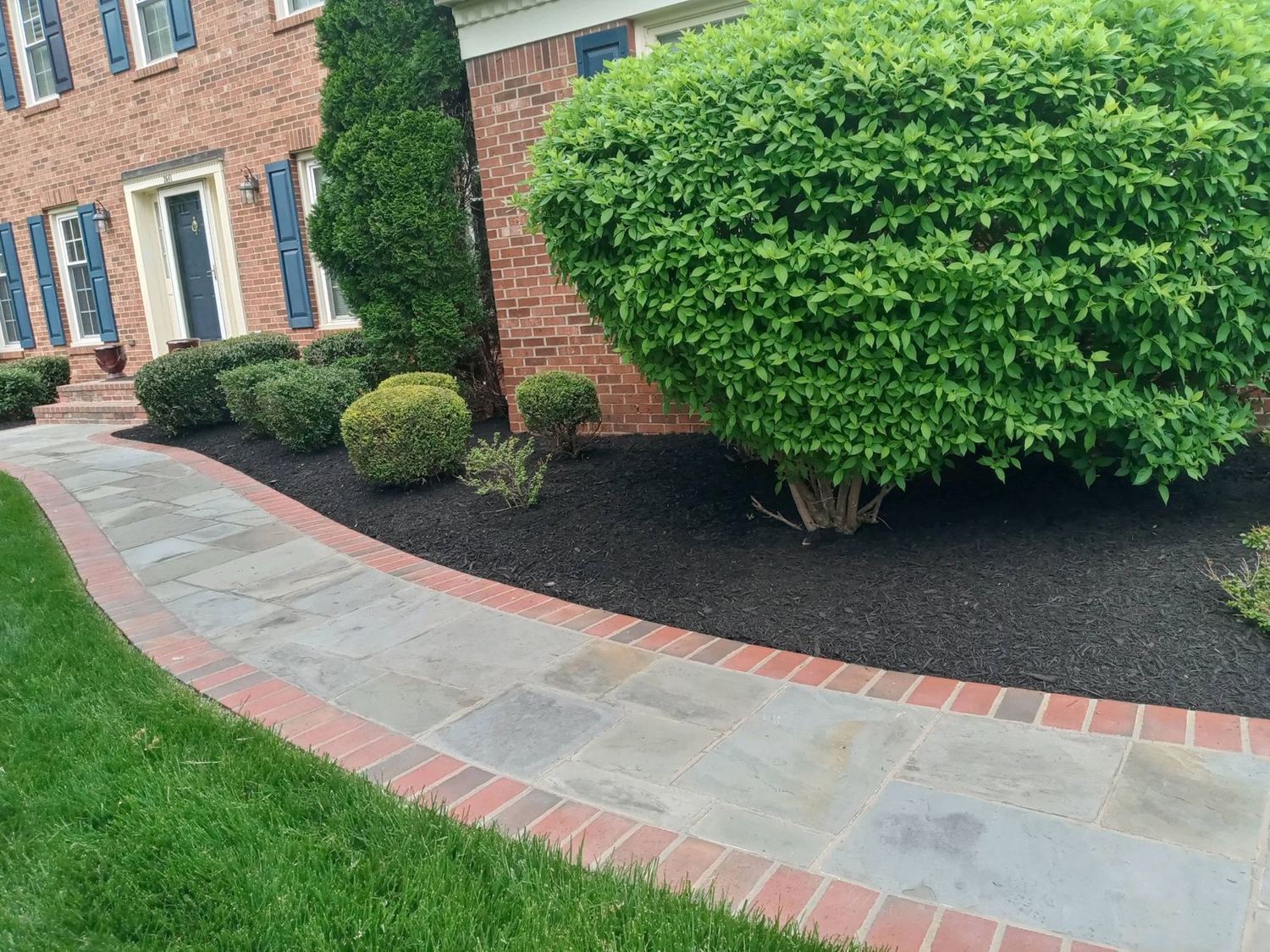 Flagstone walkway with a brick border beside freshly mulched foundation beds